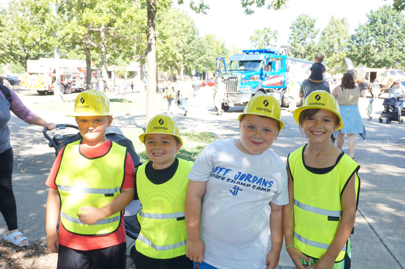 Children posing down at the Leach Amphitheater during Touch a Truck with plastic hard hats on sponsored by Oshkosh Corporation