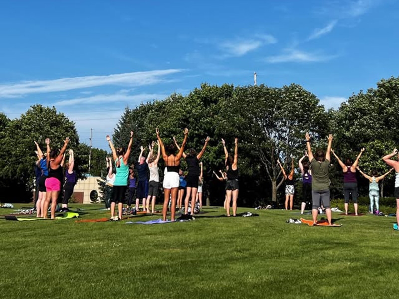 A group of people standing up stretching during a Yoga session at the Leach Amphitheater, ran by Simply Yoga
